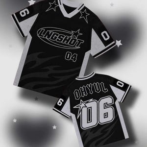 Può includere: Una maglia nera e grigia con scollo a V, grafiche a stella e la scritta LNGSHOT 04 sul davanti. Il retro mostra la scritta OHYUL 06 con grandi numeri. Entrambi i capi presentano motivi a fiamma, polsini a righe e i numeri 6 e 0.