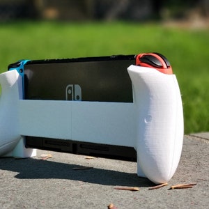May include: White 3D printed case for a Nintendo Switch console. The case has two white handles with red buttons on the right side.