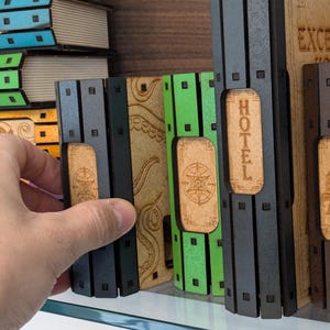May include: A set of five wooden game pieces with different colored backgrounds and designs. The pieces are labeled "Hotel", "Excelsior Hotel", and have a star and an octopus design.