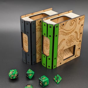 May include: Two wooden dice towers, one black and one green, with a tentacle design. The towers are shaped like books and have a slot for dice to roll out. There are five green dice on a black surface.