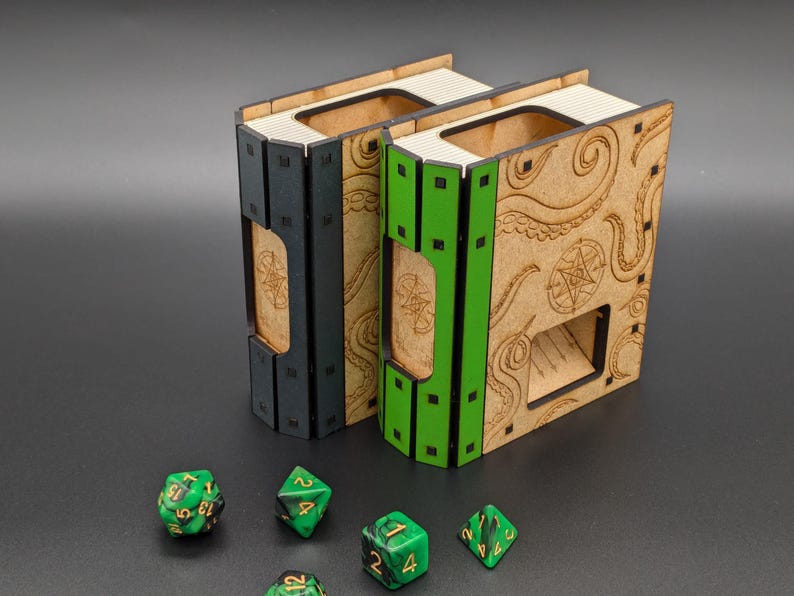 May include: Two wooden dice towers, one black and one green, with a tentacle design. The towers are shaped like books and have a slot for dice to roll out. There are five green dice on a black surface.