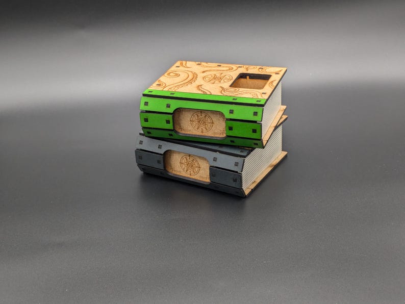 May include: Two wooden boxes stacked on top of each other. The top box is decorated with a swirling pattern and has a green stripe with black squares. The bottom box is gray with a black stripe. Both boxes have a circular design on the front.