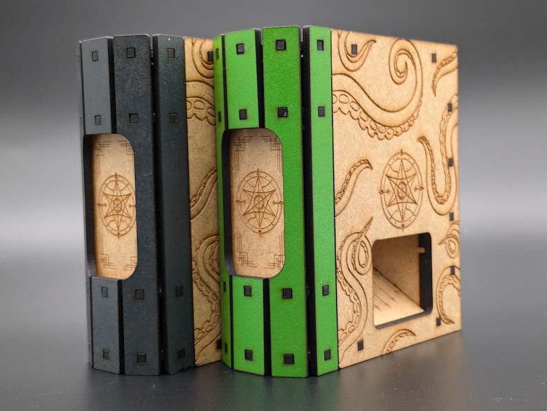 May include: Two dice towers made of wood with a black and green painted finish. The towers have a design of tentacles and a pentagram on the front. The towers are designed to hold dice for tabletop games.