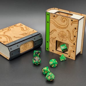 May include: Two wooden book-shaped dice towers with a tentacle design. The towers are open on the top and have a small slot for dice to fall through. Green dice are scattered around the towers.