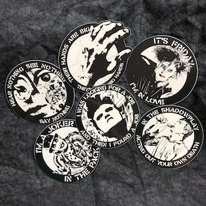 May include: A collection of black and white circular stickers with various illustrations and text. The stickers feature images of a hand, a face, and other graphic designs. Text includes phrases like "It's Friday" and "I'm in love."