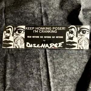 May include: Black and white bumper sticker with the text "KEEP HONKING POSER! I'M CRANKING" and "HEAR NOTHING SEE NOTHING SAY NOTHING" by Discharge. The sticker features graphic illustrations of an ear, eye, mouth, and brain.