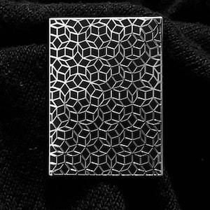 May include: A silver metal plate with a geometric pattern of repeating cubes. The pattern is embossed and creates a 3D effect.
