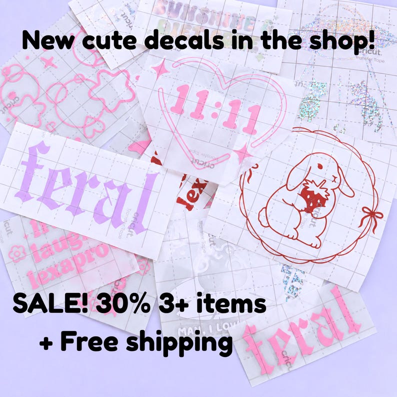 May include: A collection of various vinyl decals in pink and purple. Designs include the word "feral", a heart with the numbers "11:11", and a bunny holding a strawberry. The text "New cute decals in the shop!" is at the top.