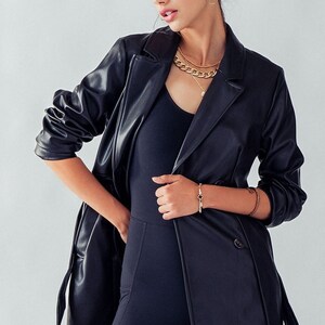 May include: A black faux leather jacket with a double-breasted closure, long sleeves, and a belt. The jacket has a relaxed fit and a slightly longer length.