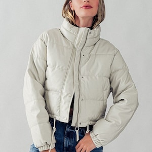 May include: A cropped white faux leather puffer jacket with a zip fastening and drawstring waist.