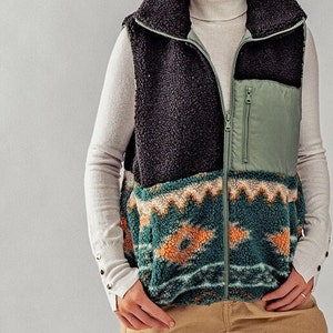 May include: A black, green, and orange patterned fleece vest with a zipper closure. The vest has a high collar and a green nylon pocket on the front.