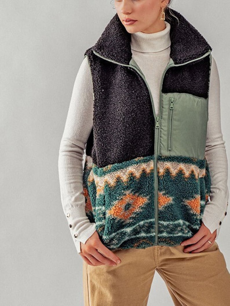 May include: A black, green, and orange patterned fleece vest with a zipper closure. The vest has a high collar and a green nylon pocket on the front.