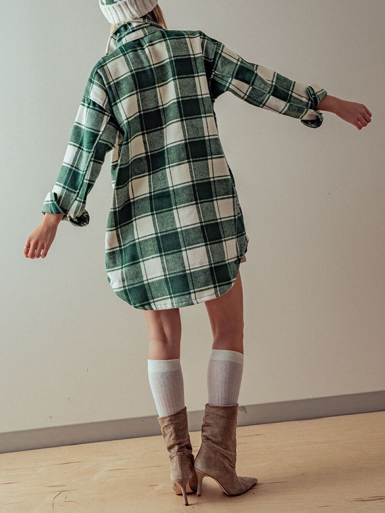 Puede incluir: Una camisa de franela a cuadros verde y blanca con mangas largas y cuello. La camisa se lleva sobre una boina de punto blanca y la modelo lleva botas de ante marr&oacute;n.