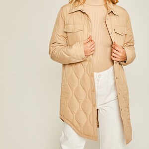 May include: A long-sleeved quilted shirt jacket in a light brown color. The jacket has a button-up front, two flap pockets, and a diamond-shaped quilted pattern.