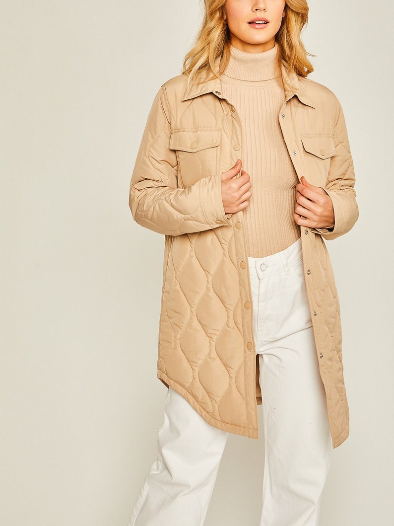 May include: A long-sleeved quilted shirt jacket in a light brown color. The jacket has a button-up front, two flap pockets, and a diamond-shaped quilted pattern.