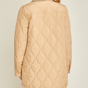 May include: A long-sleeved quilted jacket in a light beige color. The jacket has a button-up front and a diamond-shaped quilted pattern.