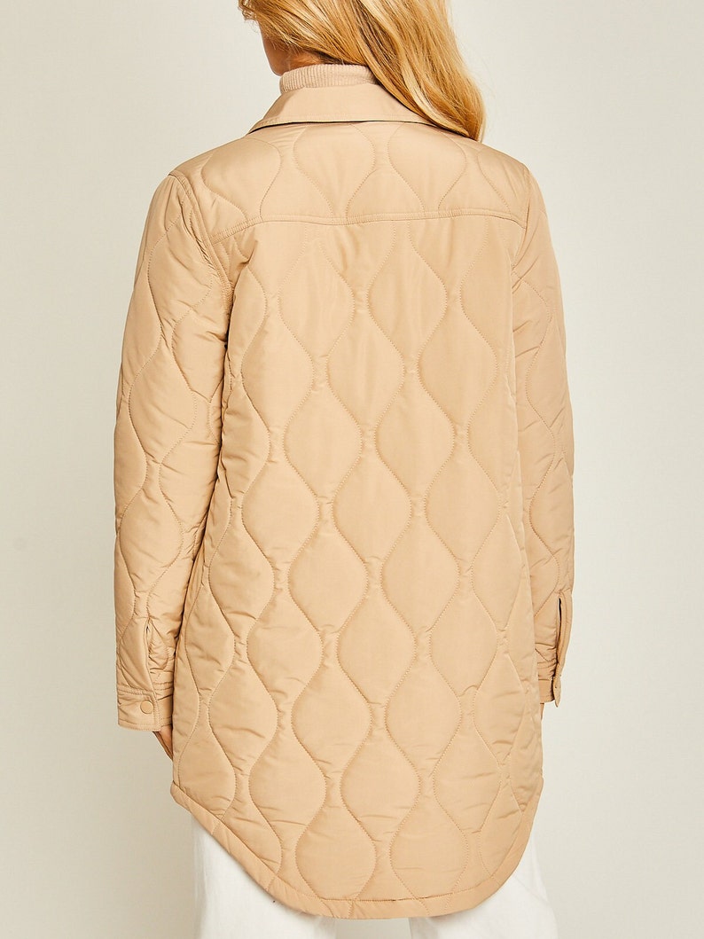 May include: A long-sleeved quilted jacket in a light beige color. The jacket has a button-up front and a diamond-shaped quilted pattern.