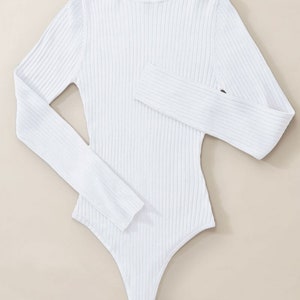 May include: White ribbed turtleneck bodysuit with long sleeves.