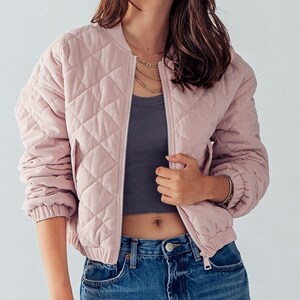 Puede incluir: Una chaqueta bomber acolchada de color rosa con cierre de cremallera. La chaqueta tiene un patr&oacute;n de rombos y es de corte corto.