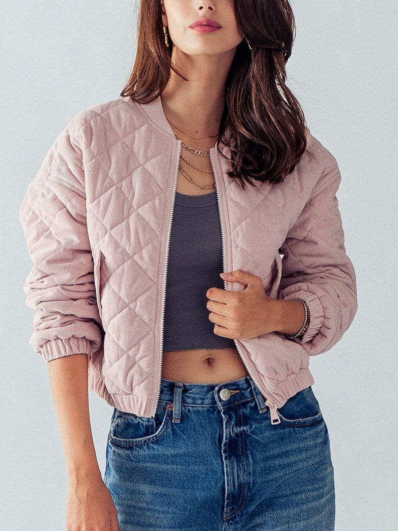 Puede incluir: Una chaqueta bomber acolchada de color rosa con cierre de cremallera. La chaqueta tiene un patr&oacute;n de rombos y es de corte corto.