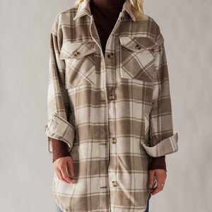 Puede incluir: Una camisa de franela de manga larga de gran tama&ntilde;o en un esquema de color beige y blanco. La camisa tiene un frente abotonado y dos bolsillos grandes con solapa.