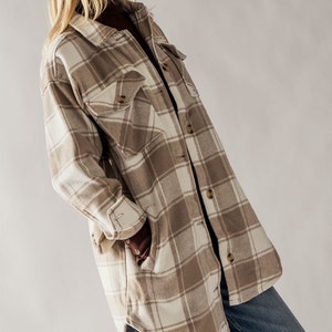 Puede incluir: Una camisa de franela de manga larga de gran tama&ntilde;o en un esquema de color marr&oacute;n y blanco. La camisa tiene un corte holgado y un dobladillo curvo.