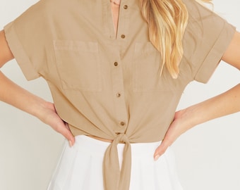 May include: A light brown, short-sleeved button-down shirt with a tie front. The shirt has a relaxed fit and is made of a lightweight fabric.