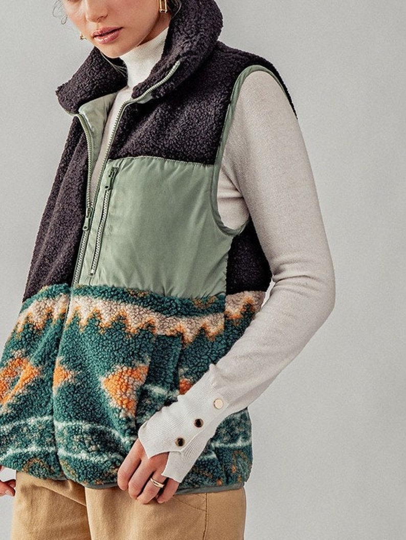 May include: A black, green, and brown patterned fleece vest with a zipper closure. The vest has a high collar and is made of a soft, fuzzy material.