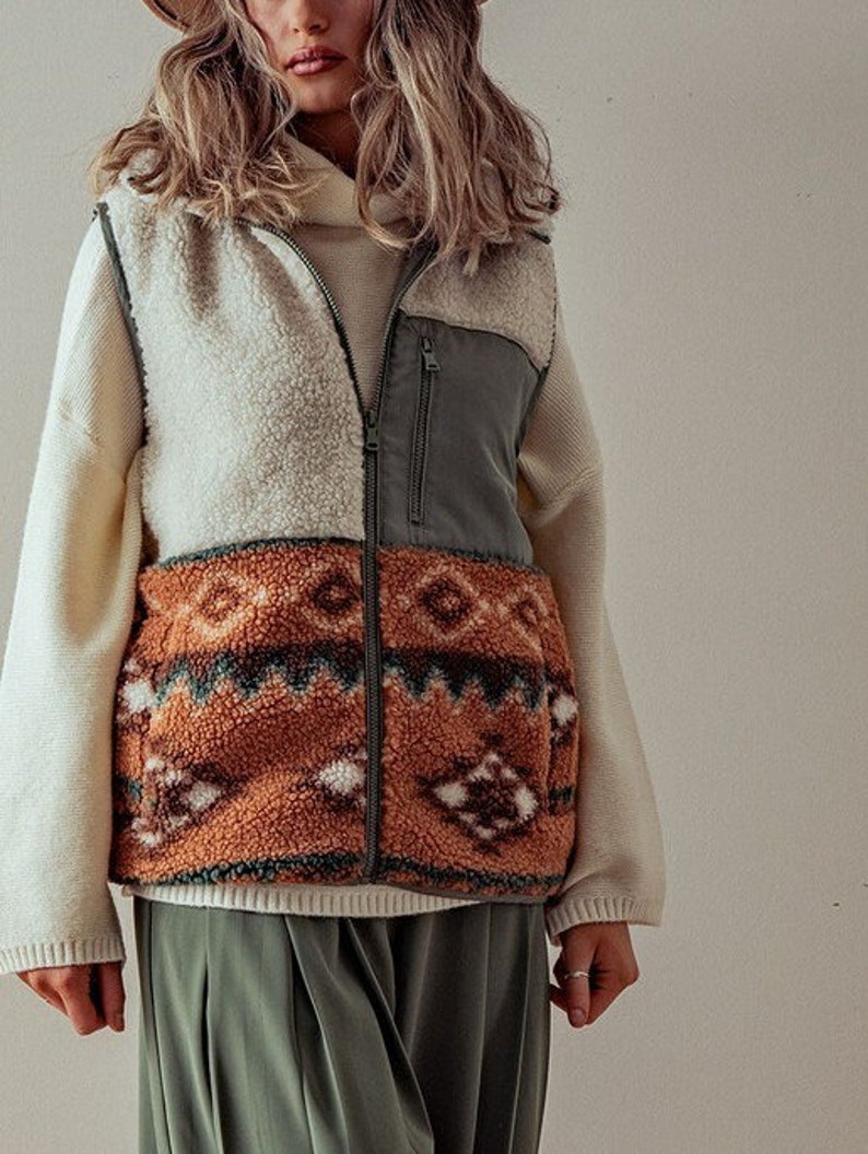 May include: A cream, brown, and green patterned fleece vest with a zipper closure. The vest has a geometric pattern on the bottom and a solid green panel on the top.