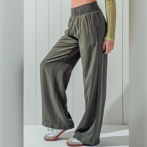 May include: Wide-leg pants in a dark olive green color with a smocked waistband. The pants are made of a soft, flowing fabric.