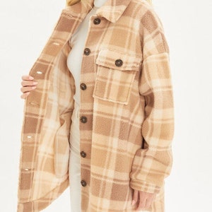 May include: A brown and cream plaid flannel shirt jacket with a soft, fuzzy texture. The jacket has a button-up front and a patch pocket on the chest.