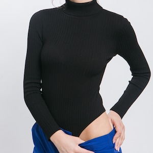 May include: A black ribbed turtleneck bodysuit with long sleeves. The bodysuit is worn with blue pants.