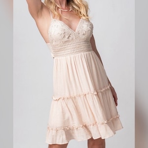 May include: A light beige sleeveless dress with a crochet bodice and tiered skirt. The dress has a V-neckline and a tie back.