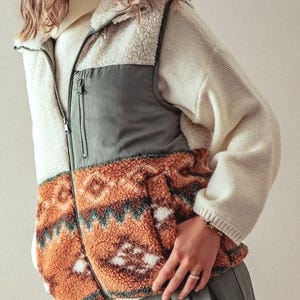 May include: A cream, green, and brown patterned fleece vest with a zipper closure. The vest has a high collar and a quilted design on the front.