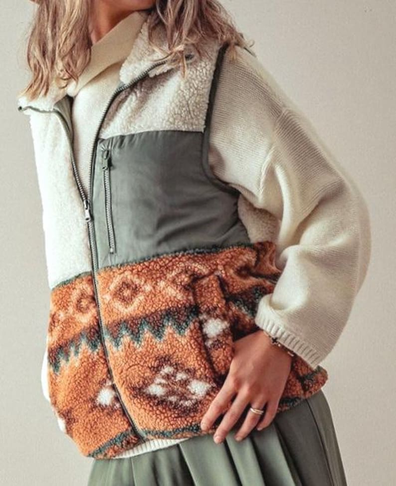 May include: A cream, green, and brown patterned fleece vest with a zipper closure. The vest has a high collar and a quilted design on the front.