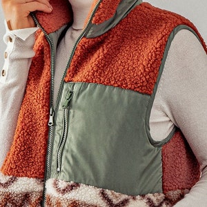 May include: A brown, green, and white sherpa vest with a zipper closure. The vest has a patchwork design with different textures.