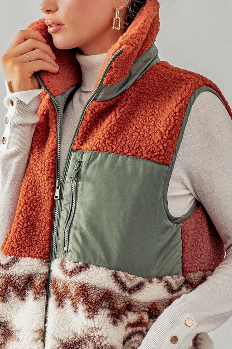 May include: A brown, green, and white sherpa vest with a zipper closure. The vest has a patchwork design with different textures.