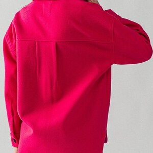May include: A bright pink, long-sleeved shirt with a collared neckline and button closure. The shirt has a relaxed fit and a slightly longer hemline.