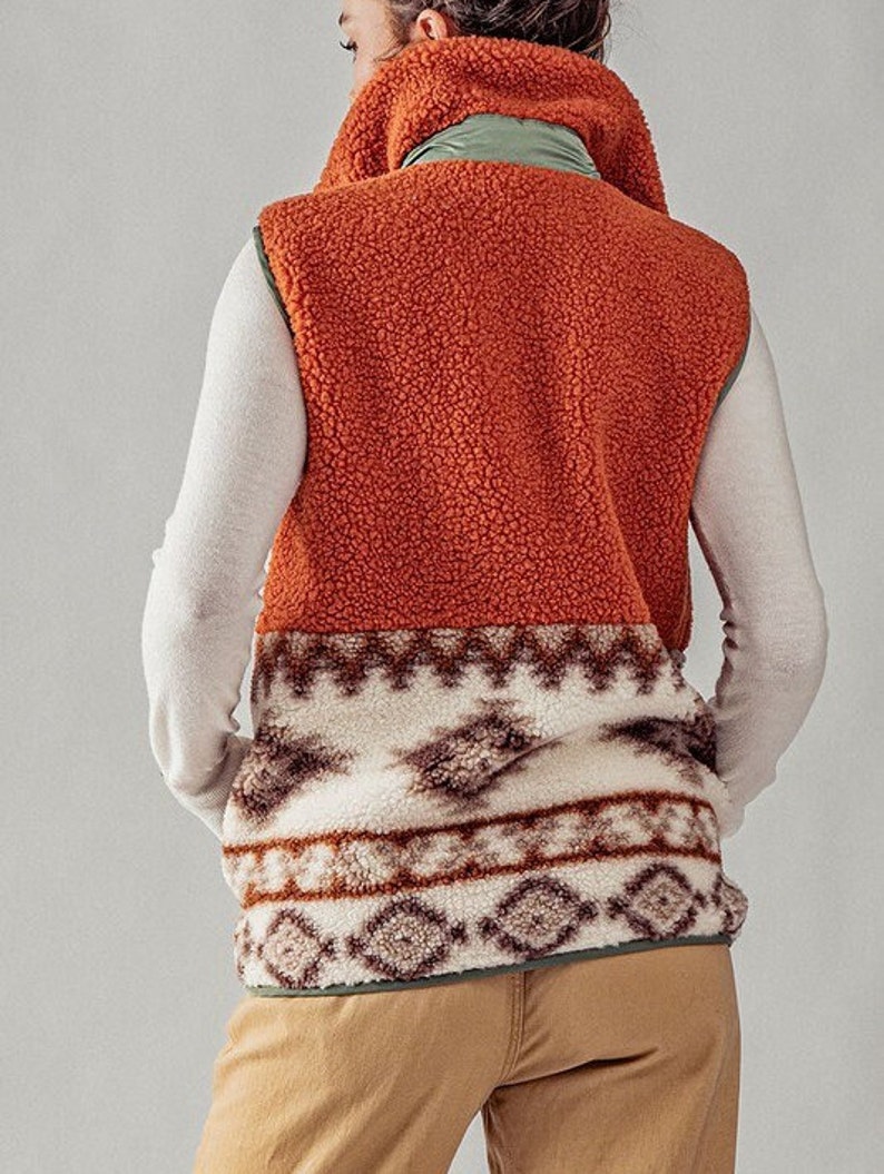 May include: A brown, orange, and white fleece vest with a geometric pattern. The vest has a high collar and a zipper closure.