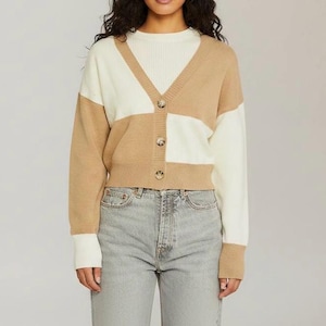 May include: A color-block cardigan in tan and white with a V-neck and three buttons. The long-sleeved sweater is paired with a white top and light gray jeans. The cardigan is a cropped style.