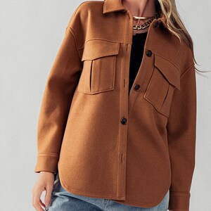 May include: A brown, long-sleeved shirt with a button-up front and two large pockets. The shirt has a relaxed fit and is made of a soft, comfortable fabric.
