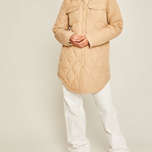 May include: A long-sleeved quilted shirt jacket in a light brown color. The jacket has a button-up front, two large flap pockets, and a relaxed fit.