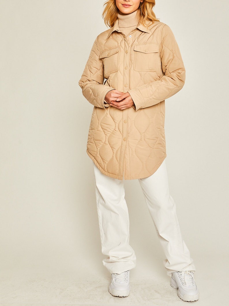 May include: A long-sleeved quilted shirt jacket in a light brown color. The jacket has a button-up front, two large flap pockets, and a relaxed fit.