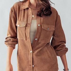 以下が含まれることがあります： ボタン留めのフロントと2つのフラップポケットが付いた、茶色のコーデュロイシャツ。シャツは長袖で、襟付きです。