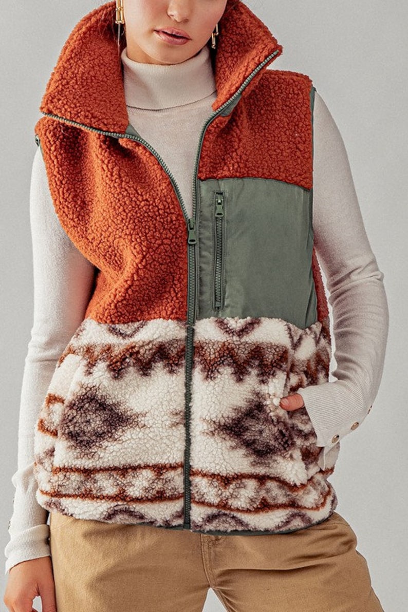 May include: A brown, green, and white patterned fleece vest with a zipper closure. The vest has a high collar and two pockets.