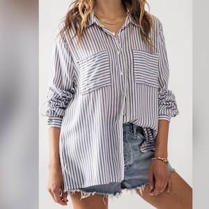 May include: A white and blue striped long-sleeve button-down shirt with two chest pockets. The shirt is oversized and has a relaxed fit.