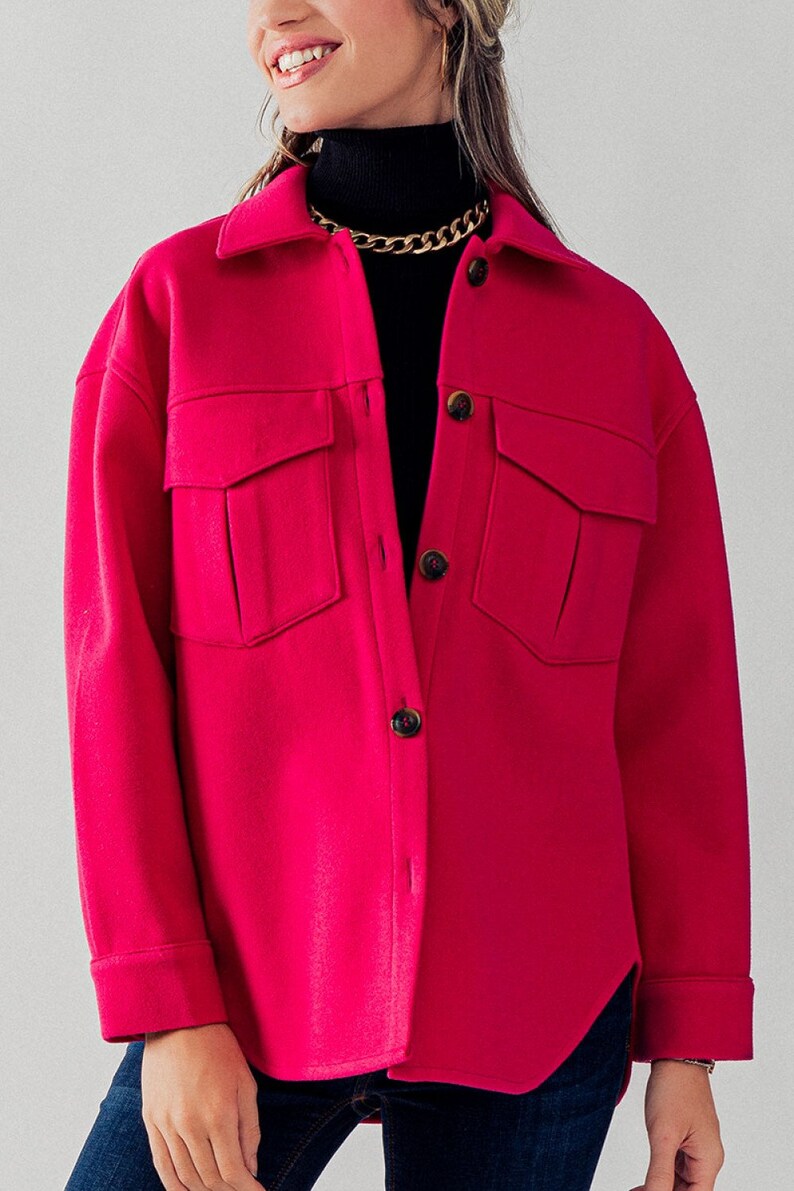 May include: An oversized button-up shirt in a bright pink colour, featuring two large flap pockets and a curved hem.