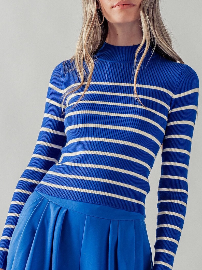Peut inclure: Un pull &agrave; manches longues bleu et blanc &agrave; rayures avec un col montant.