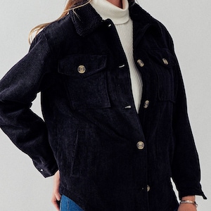 May include: A black corduroy jacket with a sherpa collar and button closure. The jacket has two flap pockets on the front and long sleeves.