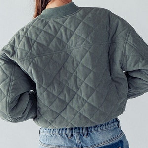 Puede incluir: Una chaqueta acolchada de pana verde con cuello alto y mangas largas. La chaqueta es corta y tiene un patr&oacute;n de acolchado en forma de diamante.